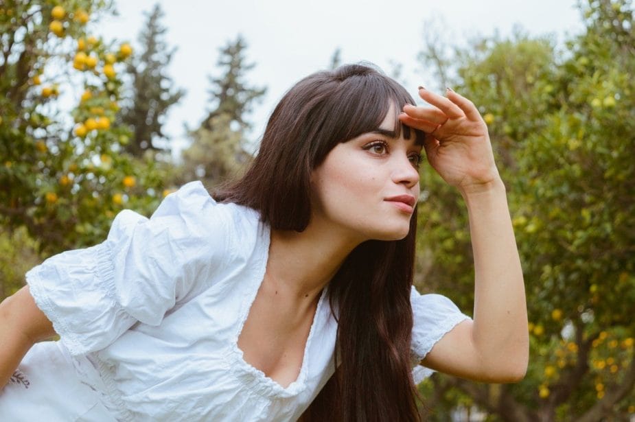 A young woman in a white dress posing in an orange orchard.